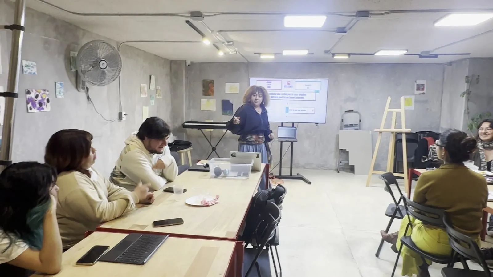 Un equipo sentado a la mesa, en primer plano, sigue la partida; al fondo están la TV y quien conduce.