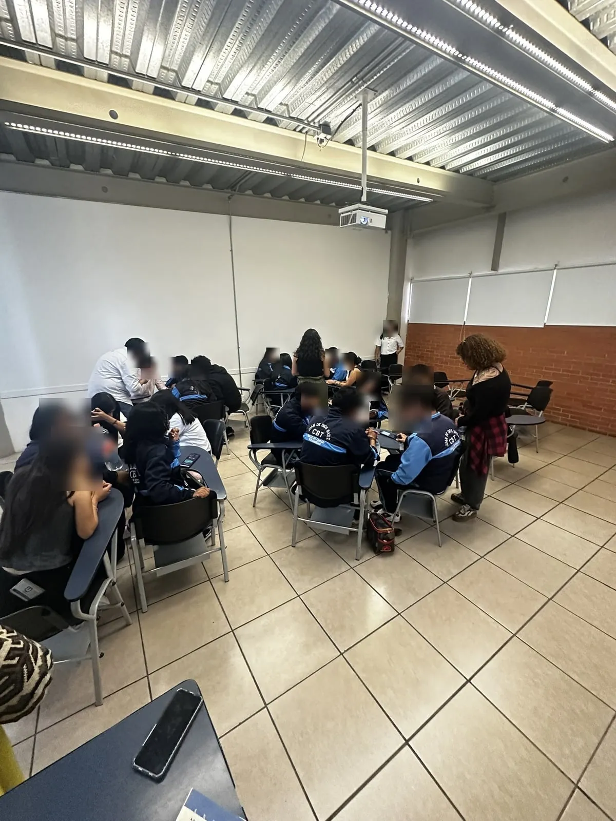 Vista amplia del salón con los equipos agrupados en sus mesas durante la partida; los rostros están difuminados.